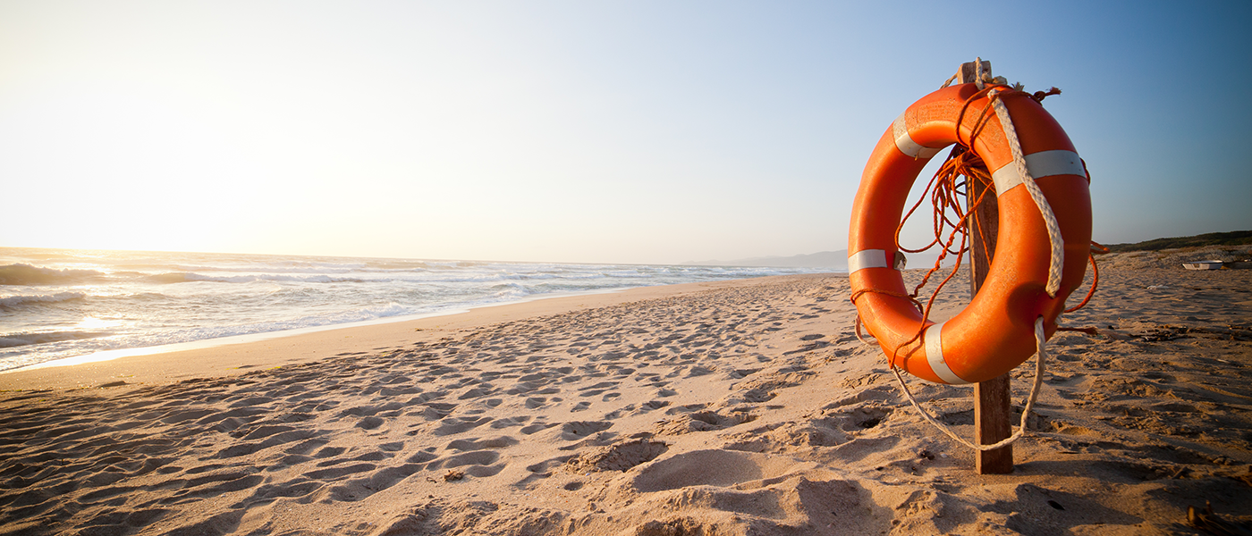 A life buoy on a beach near the ocean representing protection for you and your family. RM Mortgage Solutions can help provide protection advice.